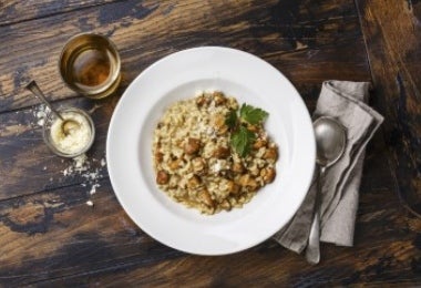 Arroz tipo arborio en plato de risotto italiano, junto con cuchara, bebida y un dip.