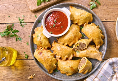 Plato de empanadas con un dip de tomate, un frito similar a los buñuelos de yuca.