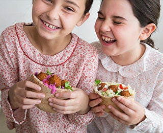 Niñas degustando alegremente pitas rellenas de falafel, un pan árabe muy similar a la foccacia italiana