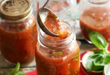 Salsa putanesca casera siendo envasada en frascos de vidrio con albahaca y tomates