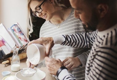 Pareja tamizando harina para preparar receta. Utensilios tamices y tazones en uso