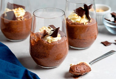 Tres vasos de vidrio rellenos de pudín de chocolate y adornados con crema batida y chocolate